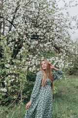 Fototapeta na wymiar beautiful girl with brown hair in a green dress in a blooming apple orchard with white flowers