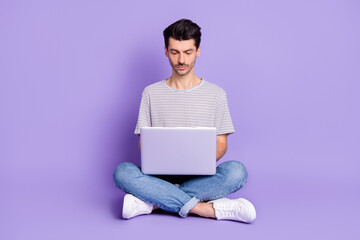 Photo of guy sit floor hold netbook look screen wear white t-shirt jeans footwear isolated purple background