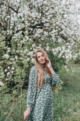 Fototapeta na wymiar beautiful girl with brown hair in a green dress in a blooming apple orchard with white flowers
