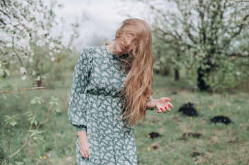 a beautiful girl with brown hair in a green dress in a blooming apple orchard her hair fluttering in the wind