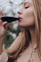 a beautiful girl with brown hair in a beige dress holds a glass of red wine in her hand in a blooming apple orchard