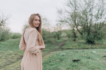 Obraz premium a beautiful girl with brown hair in a beige dress stands in the spring garden