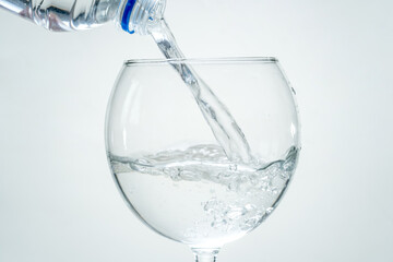 Clear healthy sparkling water is poured from a bottle into a transparent glass on a white background. Closeup