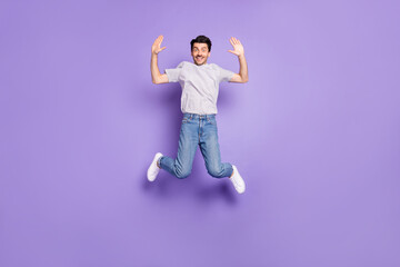 Fototapeta na wymiar Photo of funny friendly guy jump raise two hands high five wear t-shirt denim jeans sneakers isolated violet background