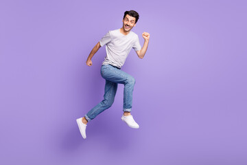 Photo of guy jump run fast look camera white smile wear black t-shirt jeans sneakers isolated purple background