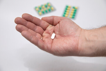 Man holding a white pill in his hand on the background of multicolored pills
