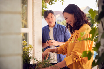 Mature Asian Couple Planting Plants Into Wooden Garden Planter At Home