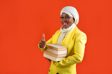 beautiful young african woman in muslim headscarf on red background with book with hand gesture 