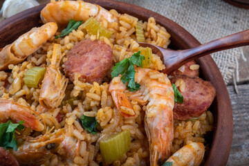 Cajun cuisine. Red jambalaya with shrimps, vegetables and sausages close-up. Selective focus. Wooden spoon.
