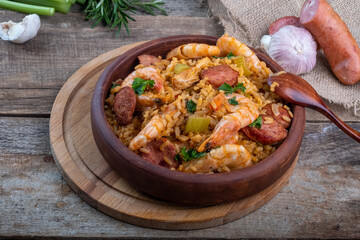 Jambalaya with shrimps and sausages on a board and wooden background.