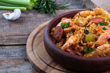 Jambalaya with shrimps and sausages on a board and wooden background. Close-up. Selective focus.