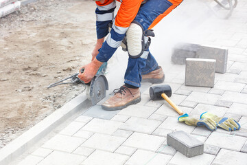 A builder uses a grinder and a diamond cutting disc to cut paving slabs in a cloud of cement dust.