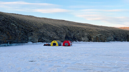 Two large winter tents with a stove stand on the ice of the frozen snow-covered Lake Baikal.