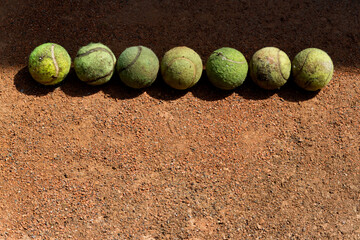 Old battered tennis balls lie in a row on clay court. Funny sports background