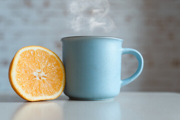 Blue mug of hot drink and orange slice on table indoors, close-up. Steam rises from the mug. Breakfast concept, good morning