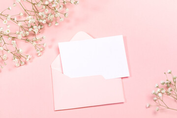 Pastel pink festive layout with envelope, empty sheet, white gypsophila flowers. Copy space for text. Mock up.