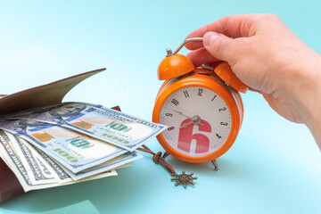Concept of vacation, travel, adventure. A hand holds an orange alarm clock and dollars in an open...