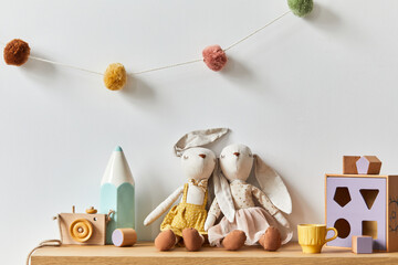 Stylish scandinavian newborn baby room with toys, plush animal, photo camera and child accessories. Cozy decoration and hanging cotton balls on the white wall. Copy space.