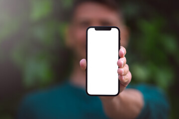 Modern smartphone mockup, blank screen. Young man showing or holding his phone with blank space outdoors on a green background