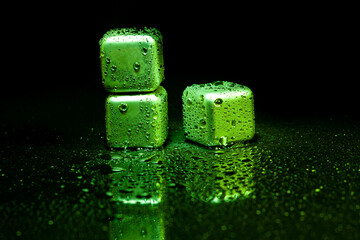 Green stainless steel cubes simulating ice for cooling drinks on a black surface with a reflection.