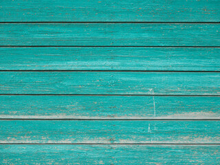 The wall is made of old horizontal boards painted. The paint color is turquoise .The paint is peeling off