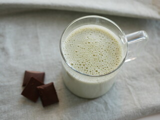 Matcha tea with milk in a transparent cup and three chocolate bars on an olive-colored tablecloth