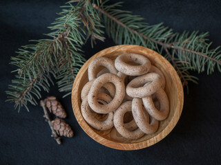 bagels in a wooden plate and a pine branch and cones next to on a black background