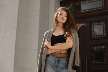 Young model woman in a trendy jacket and jeans posing on the street of a European city in the summer day