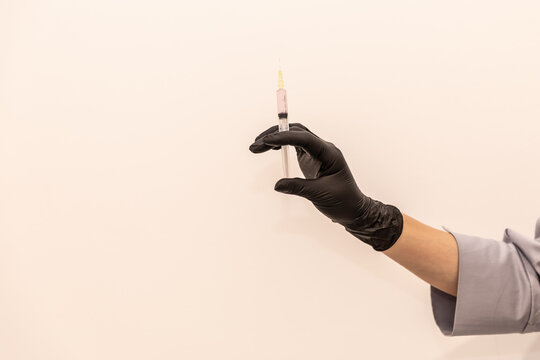 Doctor's hand in black glove with syringe.