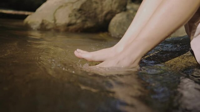 close up female soaking her feet in the canal river stream, using hands playing with water resting  freshness from nature, natural resources, feel relieve and relax, scooping natural water freshness