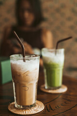 Iced cappuccino in a clear glass with milk foam on top placed on a wooden table in the cafe.