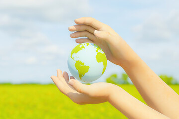 hands holding planet earth with background of green field