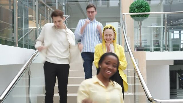 Happy young people, students, dancing down the stairs. A black African-American woman and white students have defended their diplomas, they are happy that they will receive their diplomas