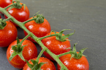 branch of small red tomatoes on black stone background. 