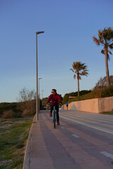 Woman in sports suit, rides a bicycle, in front of the sea, at sunset