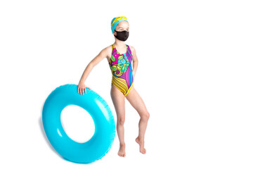 Adorable little girl in a beach swimsuit and an inflatable turquoise swimming circle, in a black protective covid-19 mask. Recreation concept during coronavirus.