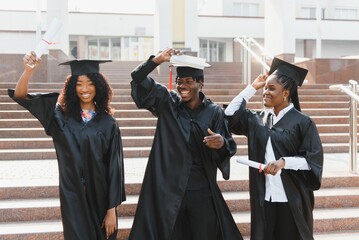 education, graduation and people concept - group of happy international students in mortar boards and bachelor gowns with diplomas