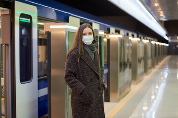 A woman in a medical face mask to avoid the spread of coronavirus is leaving the modern subway car. A girl in a surgical mask is keeping social distance on a metro station.