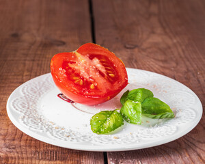 Half a red tomato and fresh basil leaves on a white plate