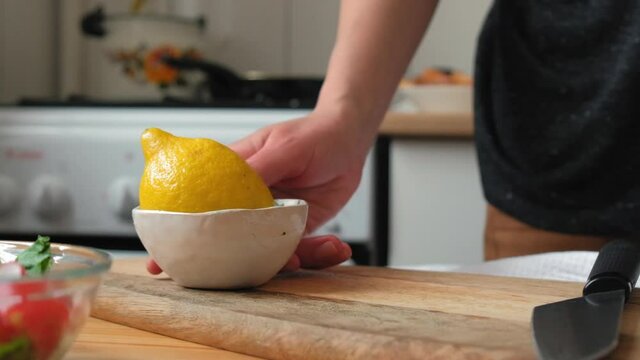 Сhef cuts yellow lemon in the kitchen on a wooden board. Female hands in a light kitchen cut a yellow lemon on the board. Сlose-up in slow motion, colorful