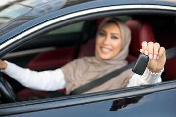 Muslim woman showing auto key, sitting on driver's seat