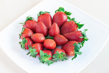 Plato de fresas sobre fondo blanco y madera