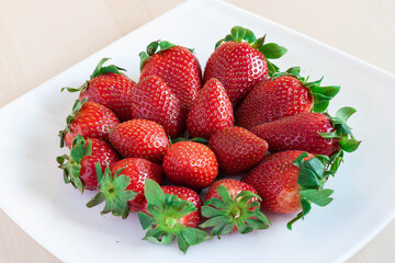 Plato de fresas sobre fondo blanco y madera