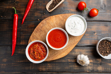 Different types of sauces in bowls on a cutting Board with garlic. On dark rustic background