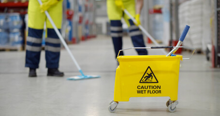 Cropped shot of worker swearing safety overall holding mop cleaning floor in warehouse