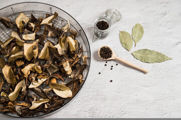 A drying dish filled with dried porcini mushrooms on a gray table. The concept of dehydration of...
