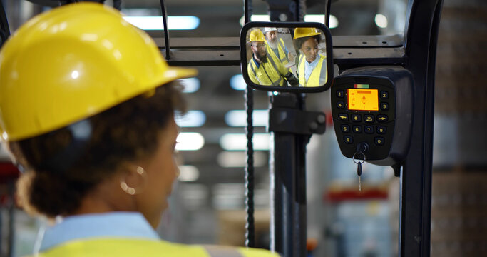 Female forklift driver sitting in truck and talking to colleagues reflected in rear view mirror