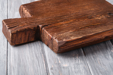 Handcraft dark brown teak wooden old cutting board, grey background, angle view selective focus