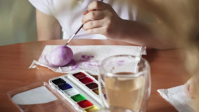 Close up of girls use paintbrushes to paint eggs . Cute little child girl wearing bunny ears on Easter day.