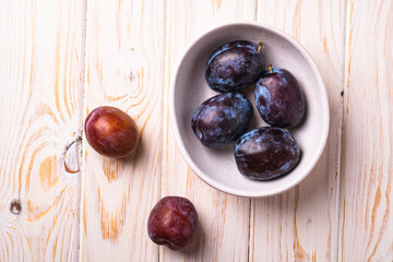 Fresh sweet plum fruits in white bowl on wood table background, top view